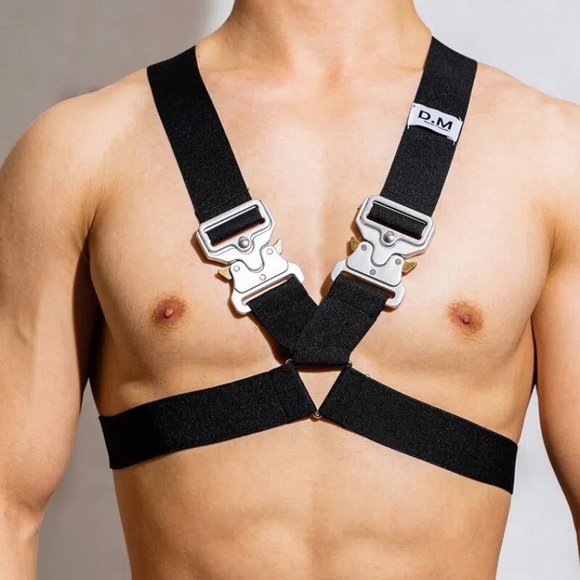 Front view of a bare torso wearing a black chest harness with silver buckles