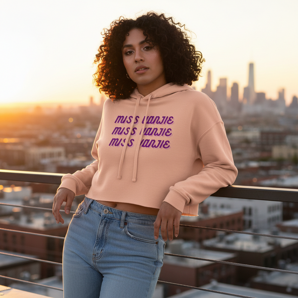Model wearing a blush pink cropped hoodie with repeated purple “MISS VANJIE” text
