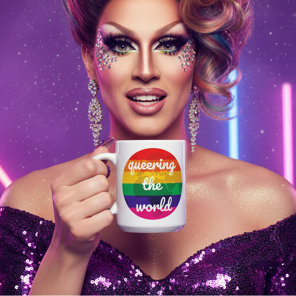 White mug with rainbow stripes and “queering the world” text held by a drag performer