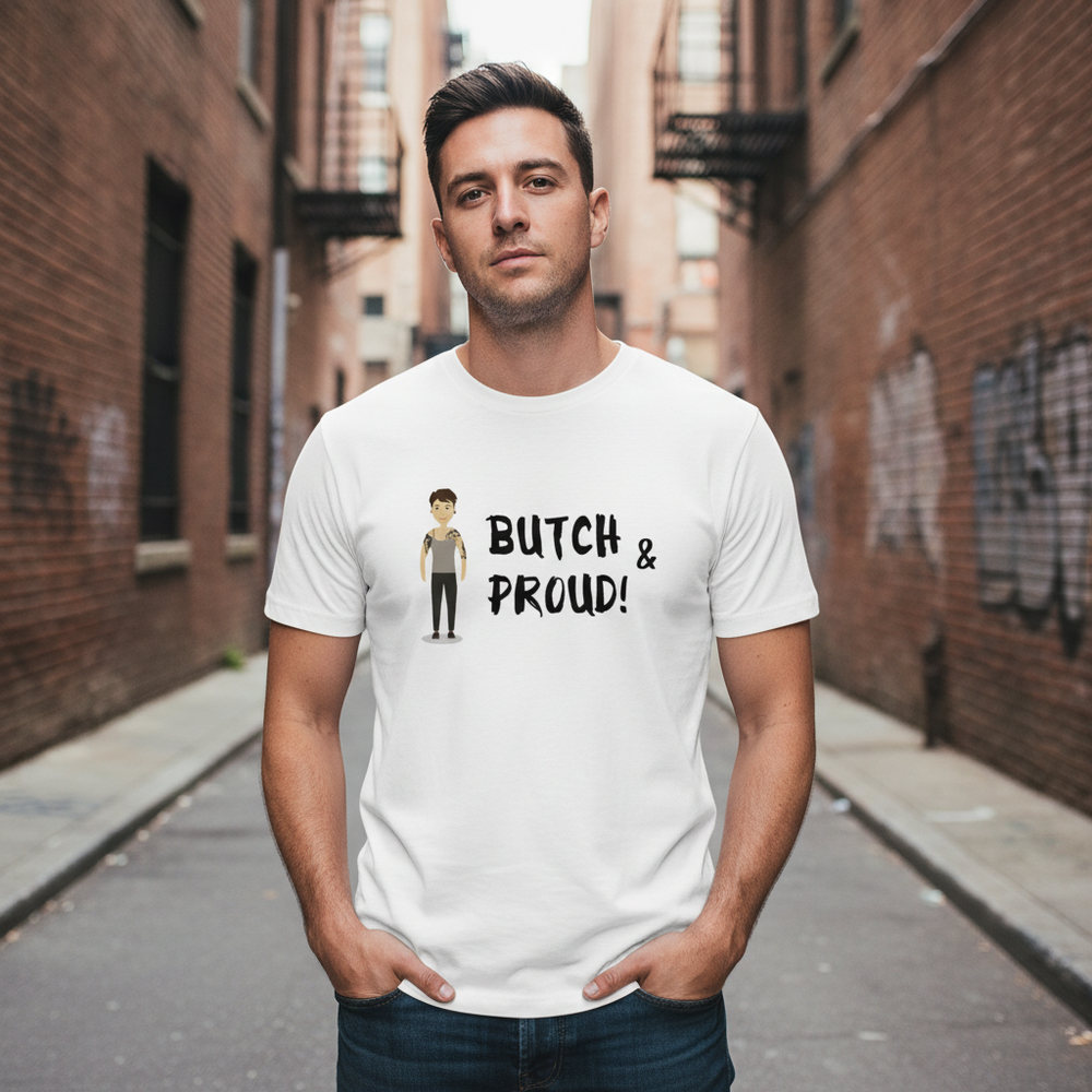White unisex Butch & Proud T-shirt with cartoon figure and “BUTCH & PROUD!” text, worn in urban alley with black graffiti.