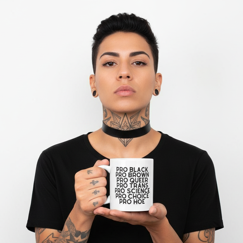 Person holding a white mug printed with “PRO BLACK PRO BROWN PRO QUEER PRO TRANS PRO SCIENCE PRO CHOICE PRO HOE”