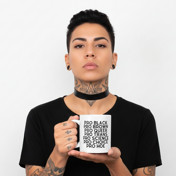 Person holding a white mug printed with “PRO BLACK PRO BROWN PRO QUEER PRO TRANS PRO SCIENCE PRO CHOICE PRO HOE”