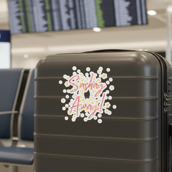 A black hard-shell suitcase at the airport, decked out with a “Sashay Away” sticker in pink cursive and yellow-white flowers.
