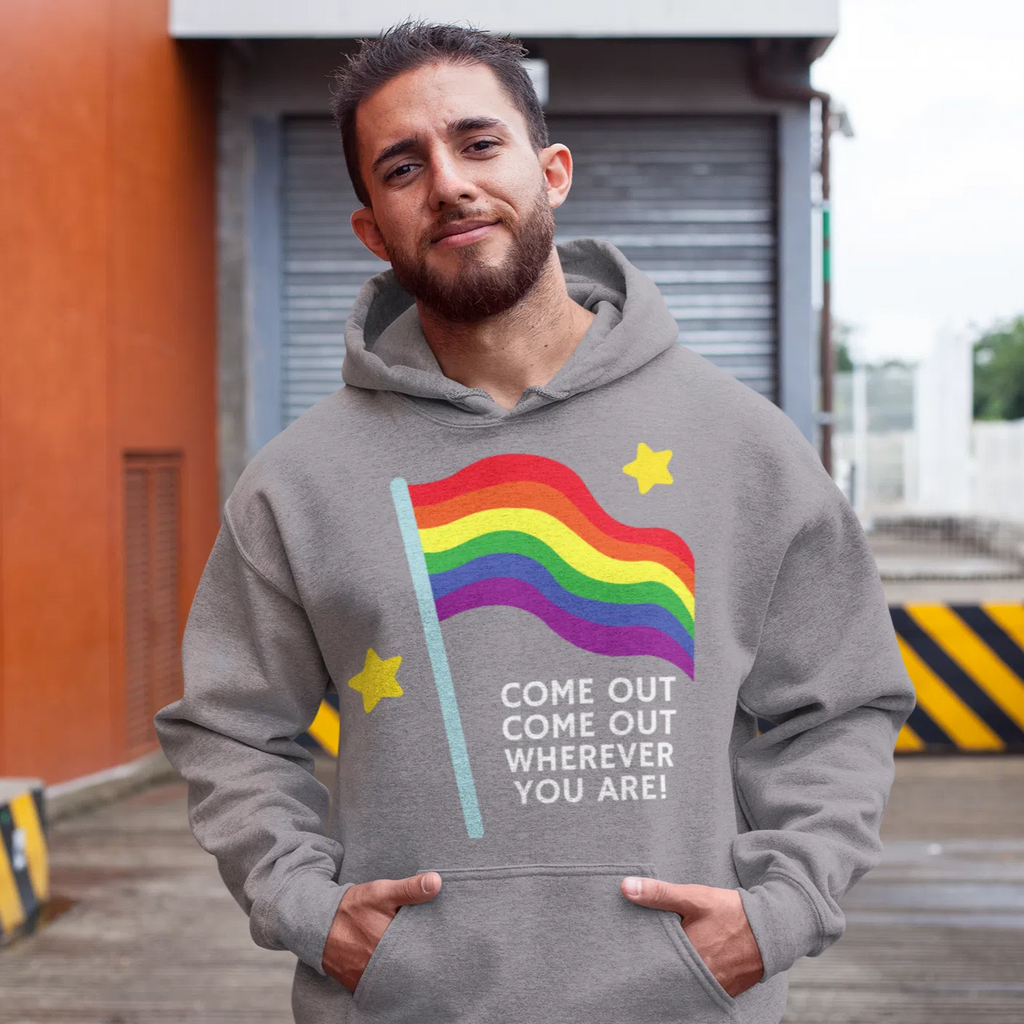 Model wearing a gray hoodie with a rainbow flag graphic and “COME OUT COME OUT WHEREVER YOU ARE!” text