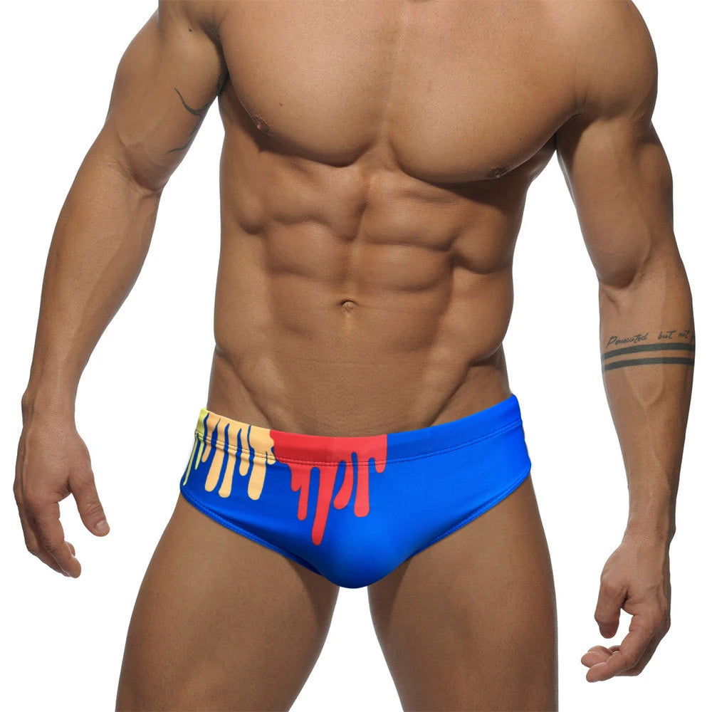 Front view of a model wearing bright blue swim briefs with red and yellow drip accents