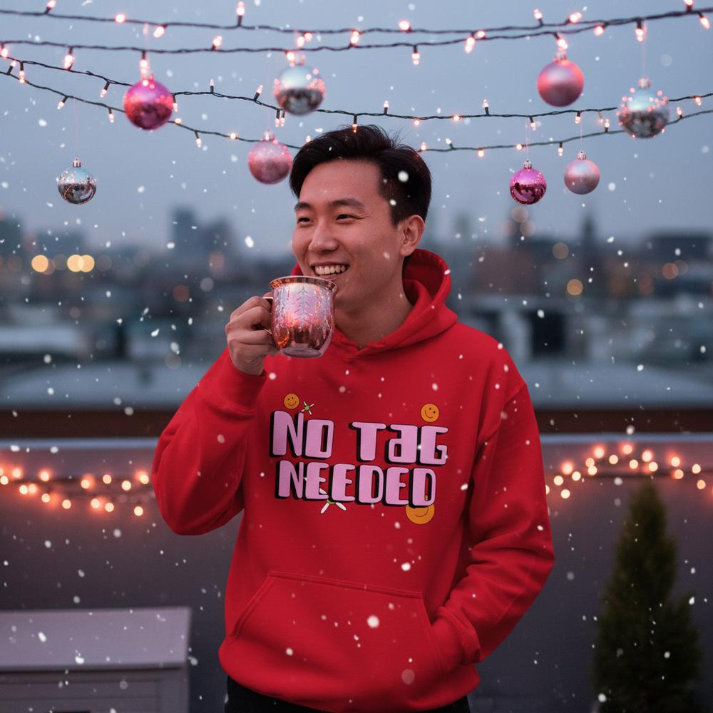 Smiling person in a red hoodie reading “NO TAG NEEDED” amid falling snow