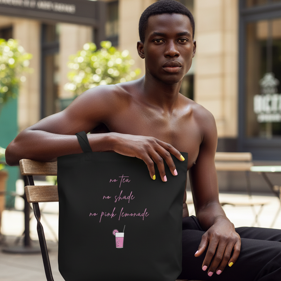 Eco tote bag—black with pink "No Tea No Shade No Pink Lemonade" script and lemonade cup. Shirtless person sitting outdoors