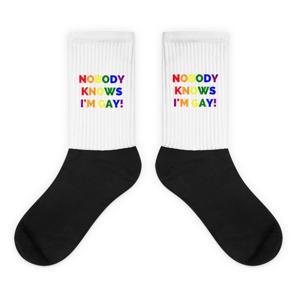 Pair of black-and-white crew socks reading “NOBODY KNOWS I'M GAY!” in rainbow letters