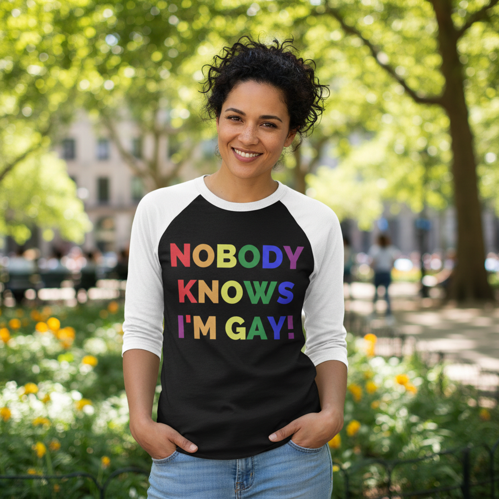 3/4 sleeve raglan shirt reads "Nobody Knows I'm Gay!" in rainbow letters; smiling wearer in sunny park with trees