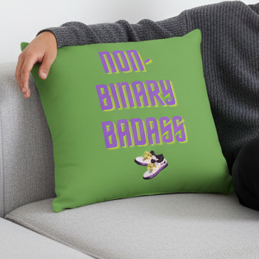 Person on light gray couch holding Non-binary Badass Pillow with bold “NON-BINARY BADASS” in purple and yellow over sneakers