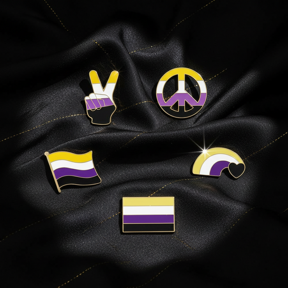 Five gold-outlined nonbinary pride enamel pins arranged on black fabric
