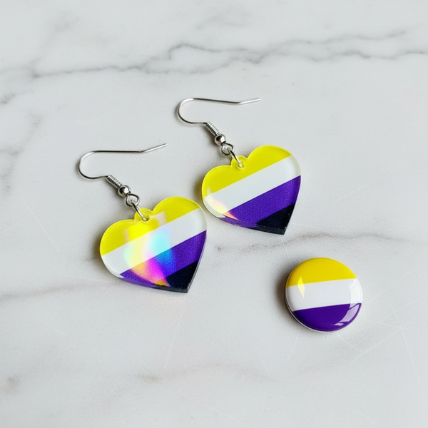 Two heart-shaped yellow, white, purple, and black dangle earrings beside a matching round pin