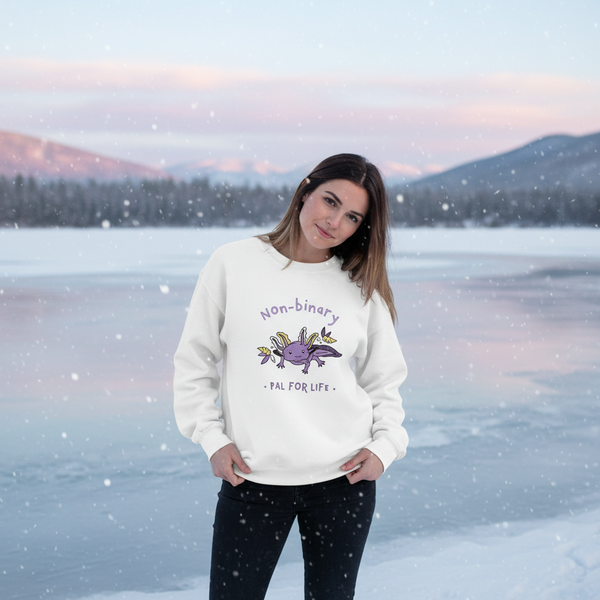 Person wearing a white sweatshirt reading “Non-binary Pal for Life” beside a snowy lake