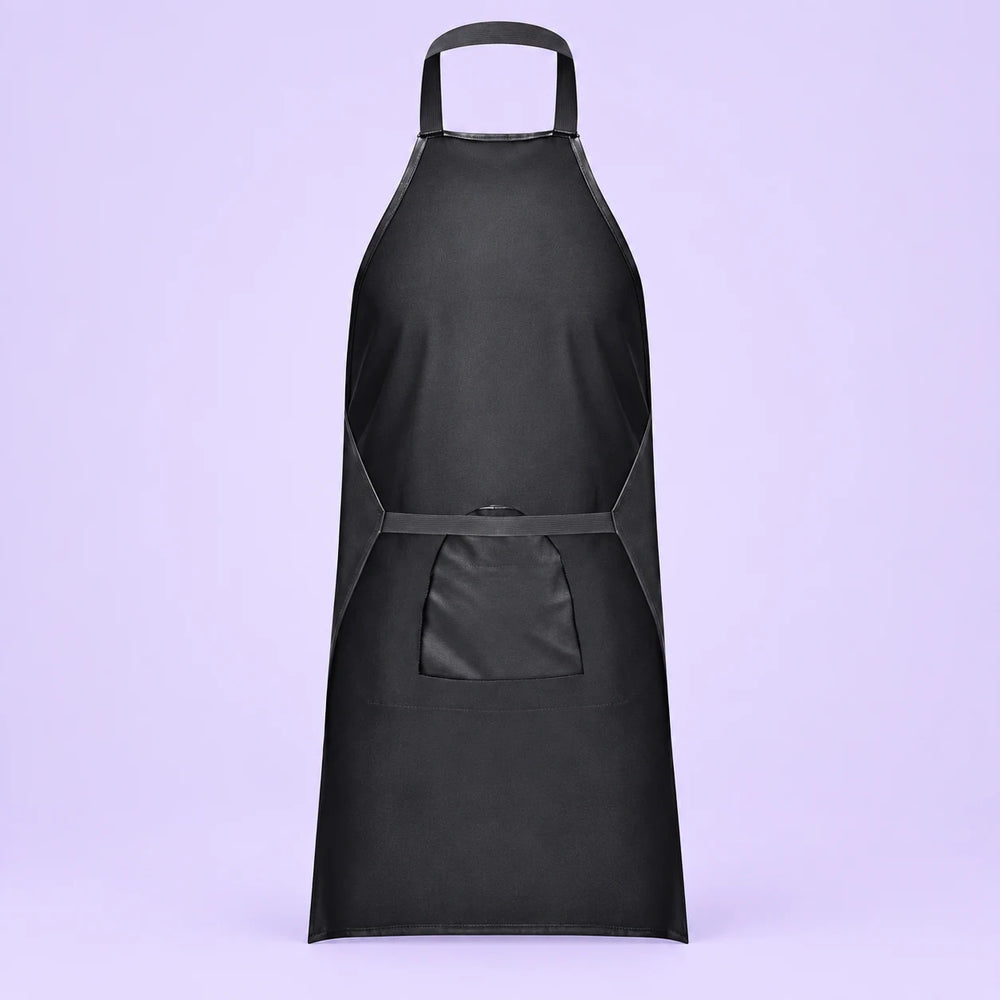 Rear view of a black leather-look apron showing its neck loop, waist strap and back of the front access panel against lavender.