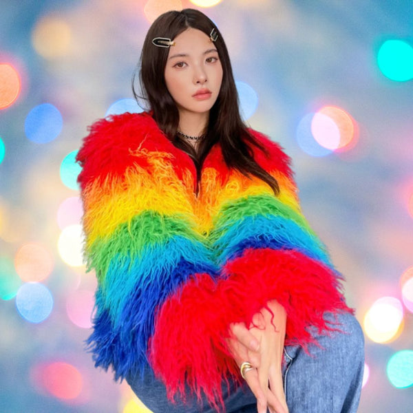 Person wearing a shaggy rainbow-striped faux-fur coat against colorful blurred lights