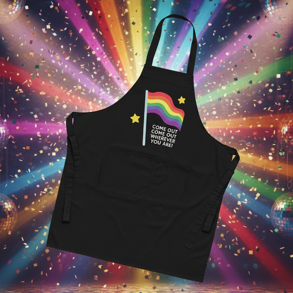 Come Out Come Out Organic Cotton Apron features a stylized rainbow pride flag with stars, bold slogan, large pocket, neck loop, and waist ties, embodying queer pride and self-expression in the kitchen.