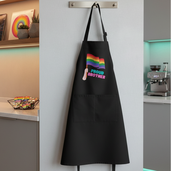 Proud Brother Organic Cotton Apron with a waving rainbow Pride flag graphic, displayed on a modern kitchen wall hook, embodying LGBTQIA+ pride and self-expression.