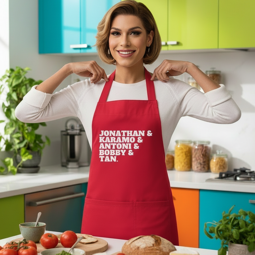 Person proudly dons the Jonathan & Karamo & Antoni & Bobby & Tan Organic Cotton Apron in a vibrant kitchen, surrounded by cooking ingredients, embodying queer pride and culinary confidence.