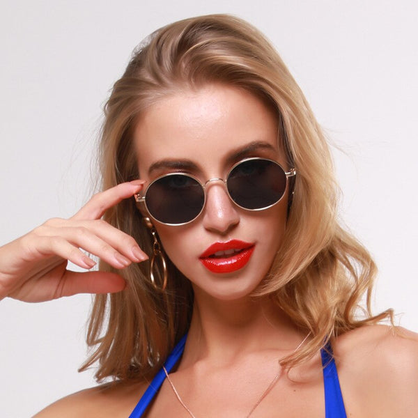 Model wearing round black-lensed sunglasses with thin silver frames, touching the left temple