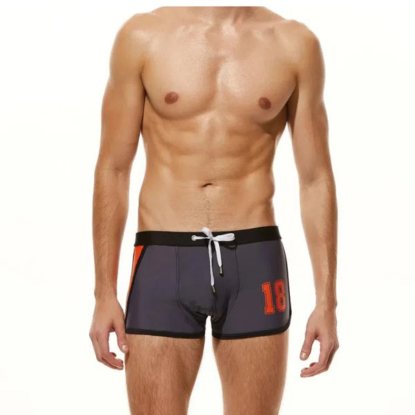 Front view of a model wearing dark boxer-style swim trunks with orange accents and number 18