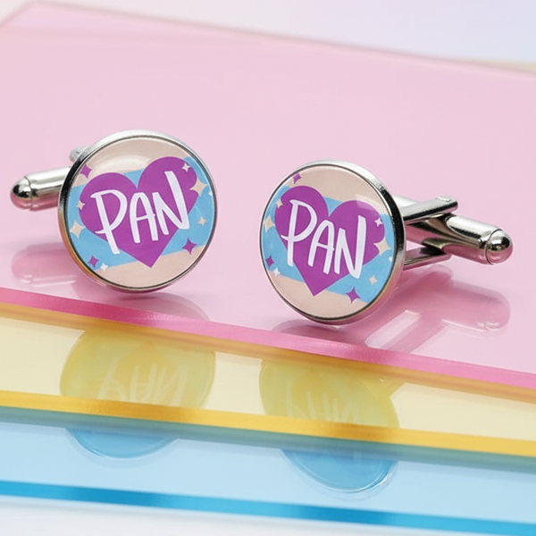 Pair of silver cufflinks reading “PAN” over purple hearts on a pink surface