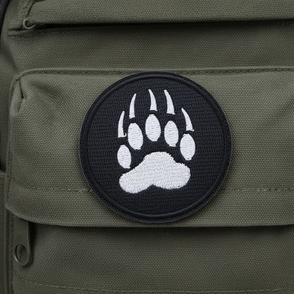 Paw Print Iron-On Embroidered Patch with bold black bear paw and claws, outlined in black, on olive green fabric.