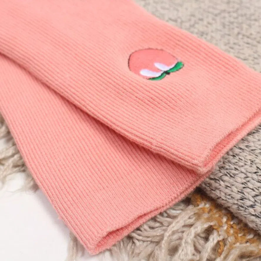 Close-up of peach-pink ribbed socks with a small peach-shaped embroidered motif