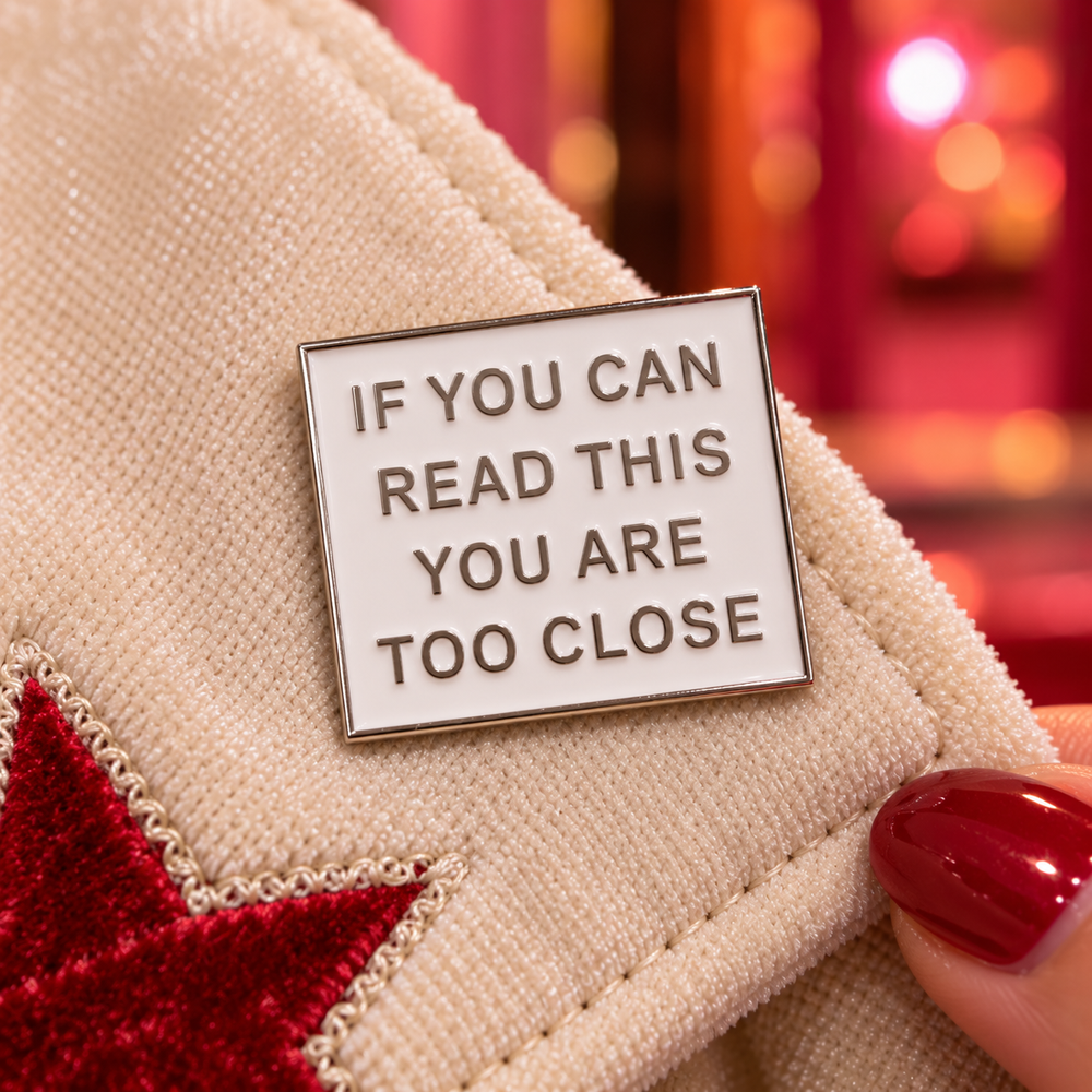 If You Can Read This You Are Too Close Pink Enamel Pin in White, styled at a bubblegum-pink venue entrance with worn timber steps, a chrome handrail and soft evening light.