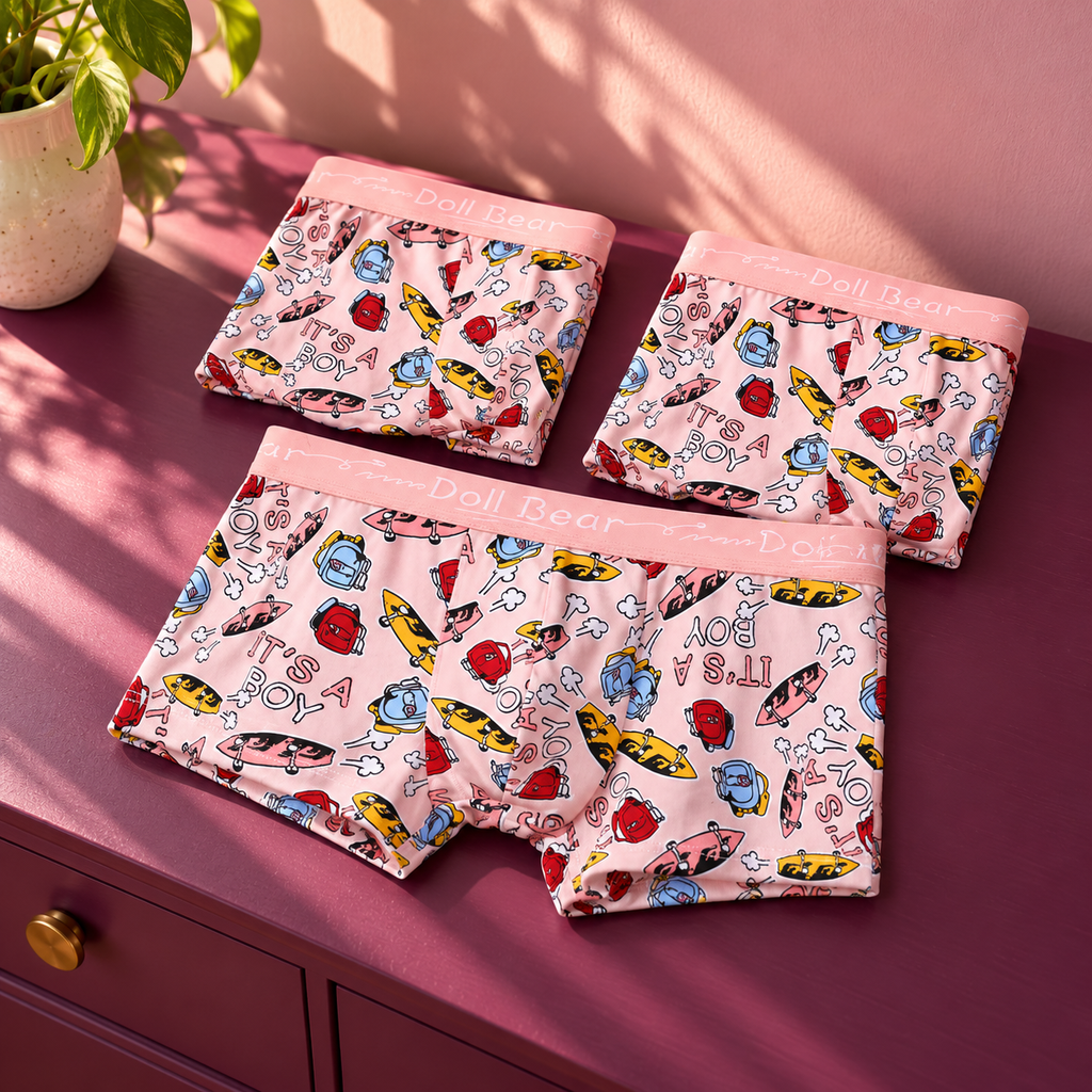 Three matching pairs of pink Doodle cotton boxer briefs with pink waistbands arranged on a plum dresser.