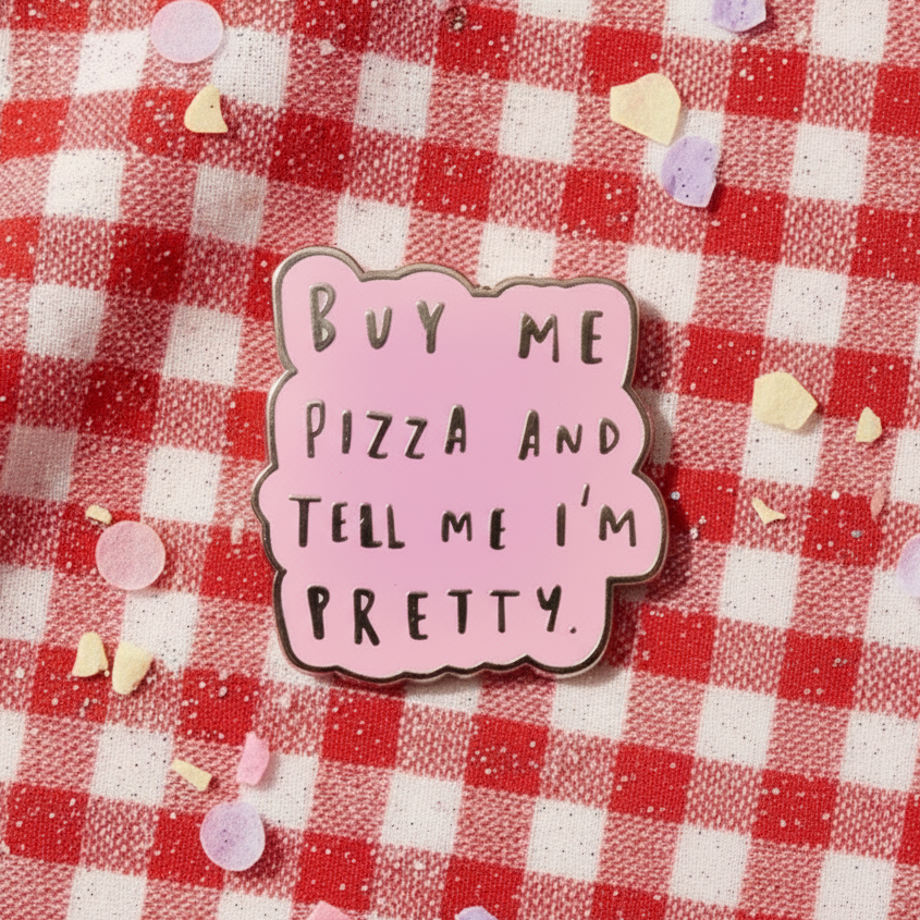 Pink enamel pin reading “Buy Me Pizza and Tell Me I'm Pretty” on red gingham fabric