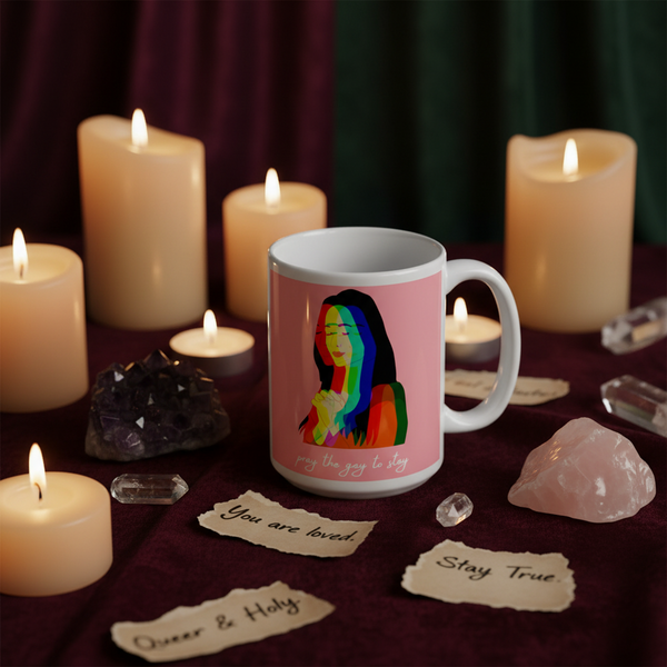Pink mug with rainbow portrait and “pray the gay to stay” text among lit candles and crystals