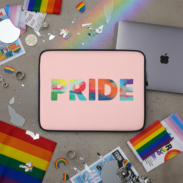 Pink Pride laptop sleeve with “PRIDE” in rainbow letters, shown on gray surface with rainbow flags, unicorn stickers, rings