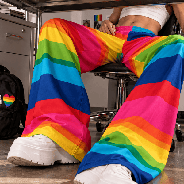 Seated model wearing bright rainbow-striped palazzo pants with wide legs and white sneakers