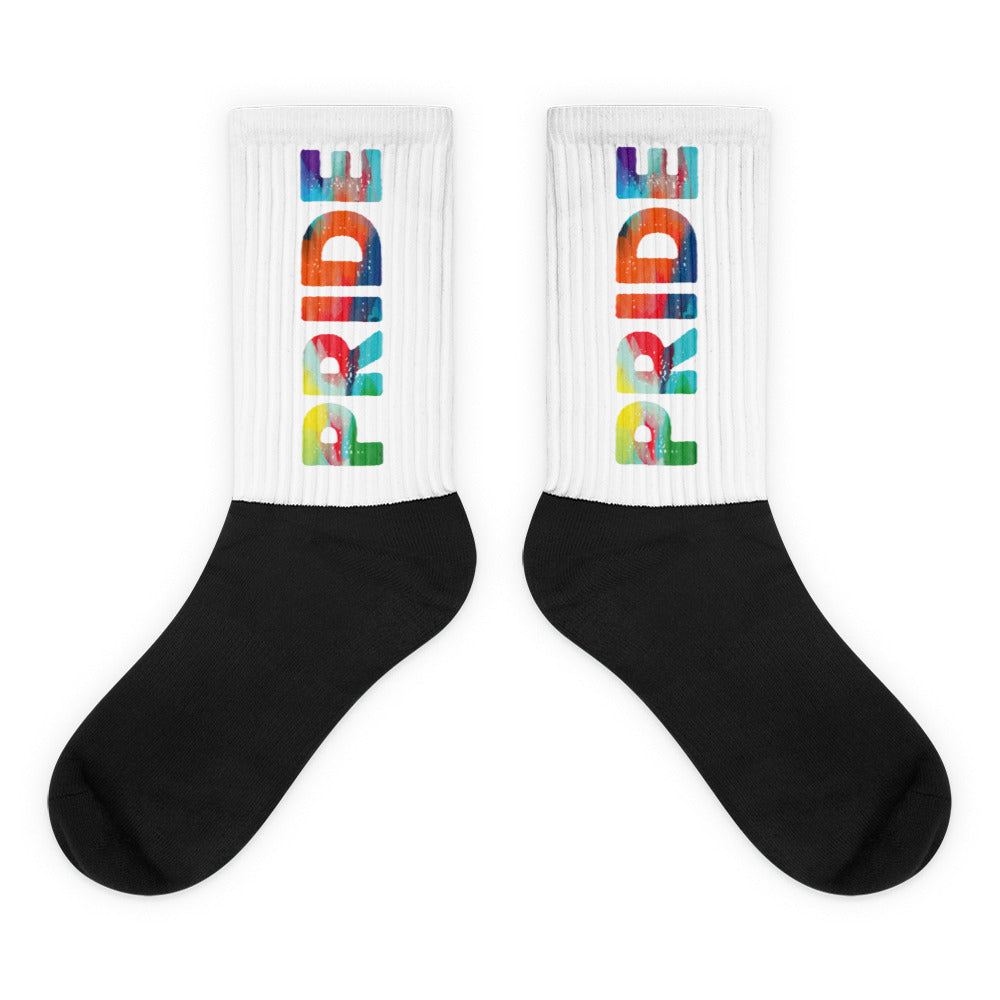 Pair of crew socks with black feet and white cuffs spelling PRIDE in rainbow letters