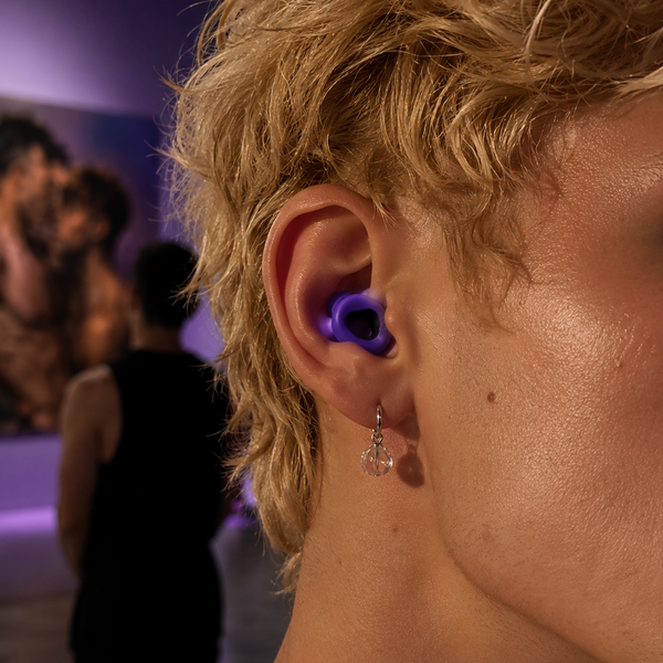 Close-up side view of a purple earplug worn in a person's ear at an indoor gathering