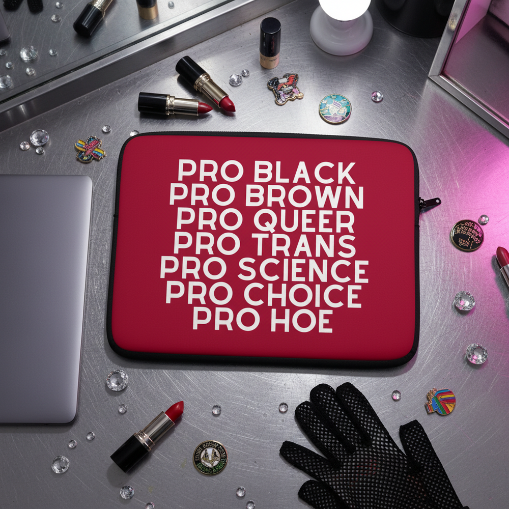 Red Pro Hoe laptop sleeve with bold white “PRO BLACK, PRO BROWN, PRO QUEER...” text on vanity with makeup, pins, mirror