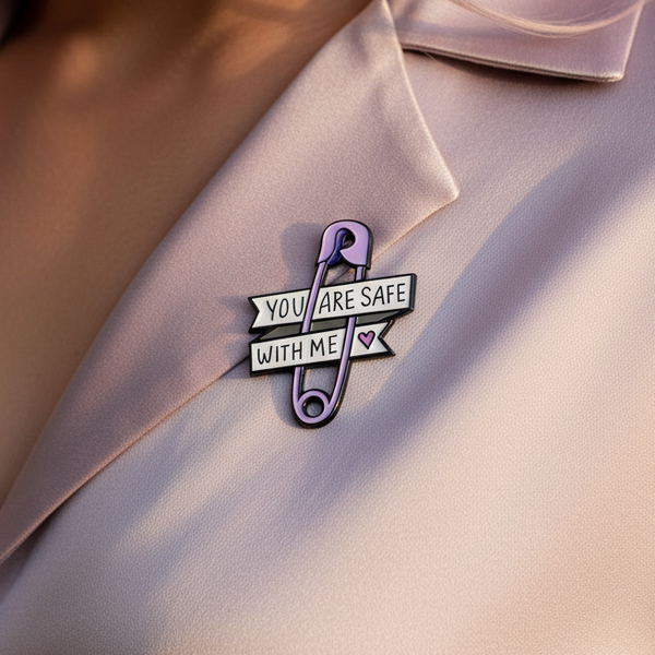 Close-up of a lavender safety-pin enamel pin reading “YOU ARE SAFE WITH ME”