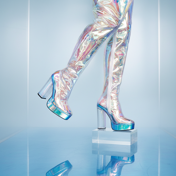 Translucent PVC high heel boots with a slick, iridescent rainbow sheen, worn for a pride vibe; only legs and feet showing.