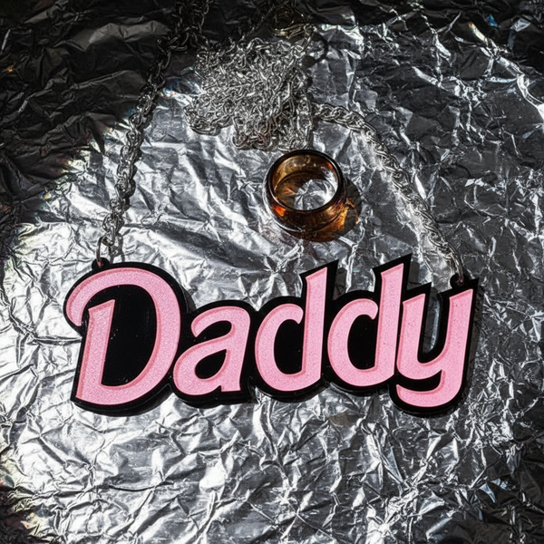 Close-up of a pink acrylic “Daddy” statement pendant on a silver chain