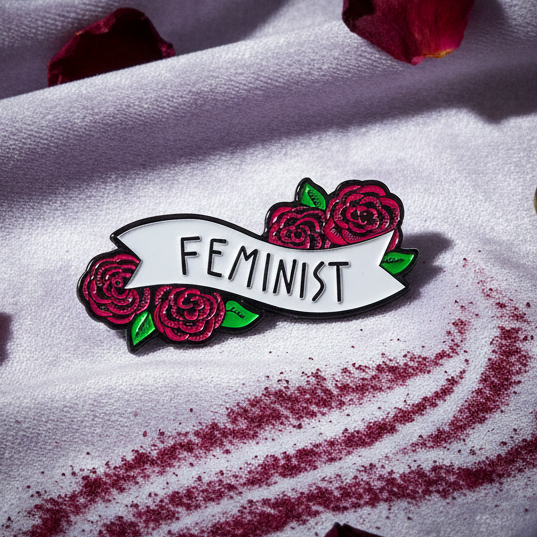 Close-up of a feminist enamel pin with red roses and green leaves on a white banner