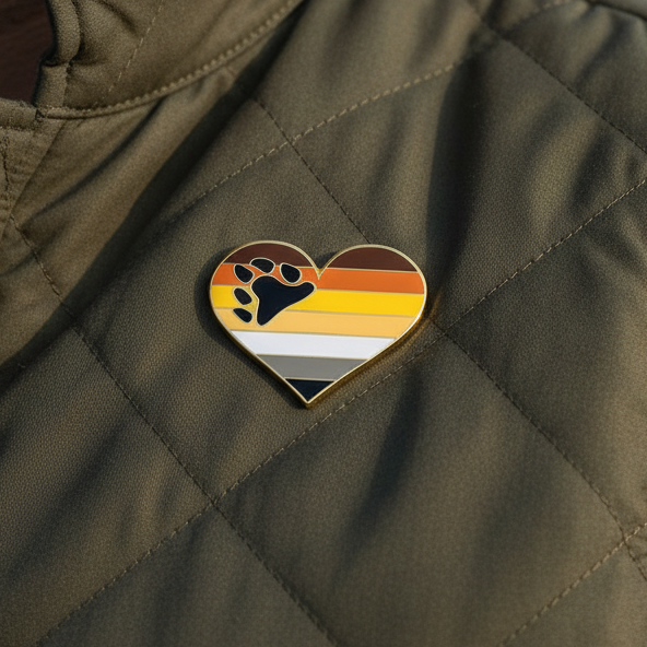 Bear Pride Heart Enamel Pin on a quilted olive-green jacket, featuring stripes of the bear pride flag and a black paw print, embodying fierce LGBTQIA+ pride and joyful self-expression.