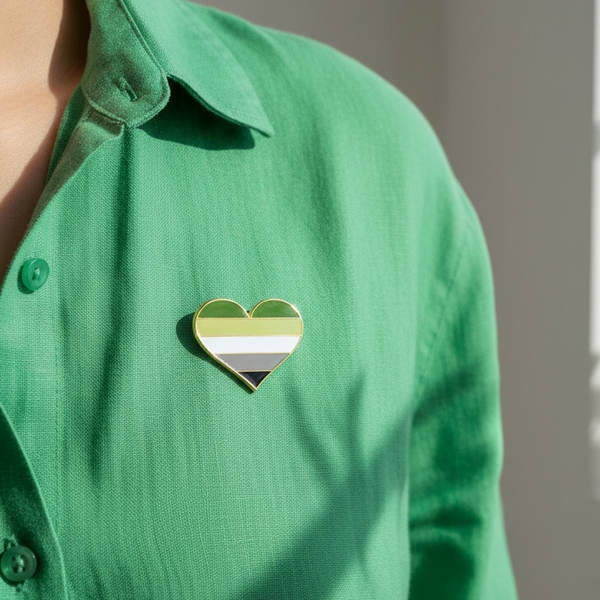Aromantic pride heart enamel pin worn on a green button-up shirt