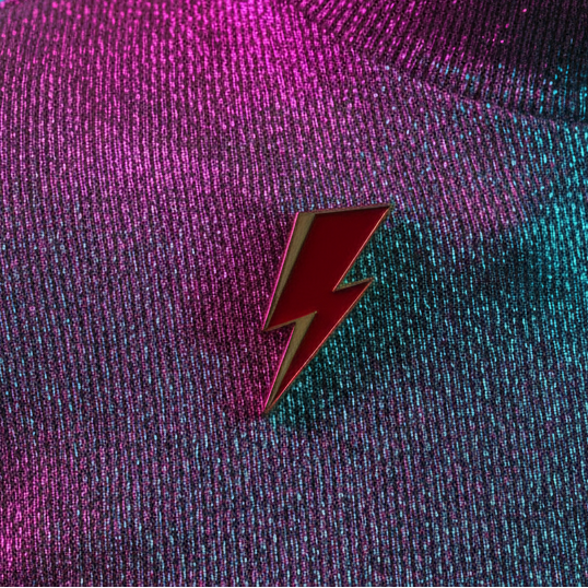 Red lightning bolt enamel pin on shimmering magenta and teal fabric