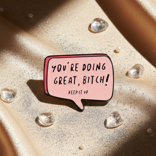 You're Doing Great Bitch Enamel Pin: A pink speech-bubble pin with bold black lettering on gold fabric, surrounded by glistening beads, celebrating fierce queer pride and self-expression.
