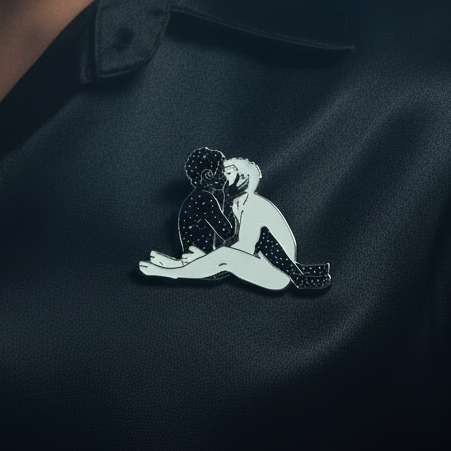Close-up of a black-and-white enamel pin showing two men kissing beneath stars
