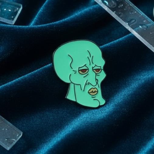 Squidward enamel pin with a green cartoon face on dark blue fabric