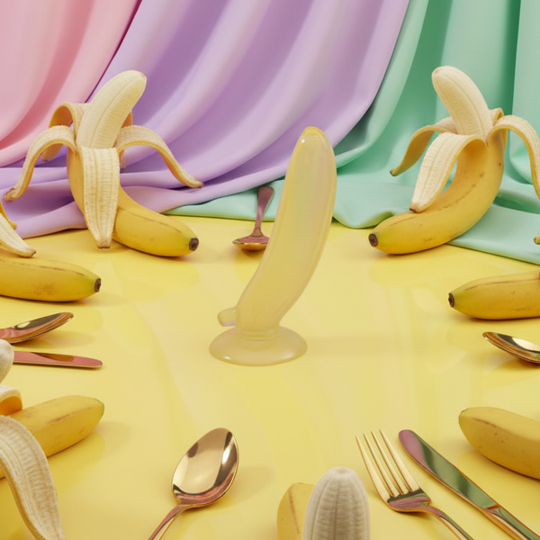 Banana-shaped dildo standing upright on a suction base among bananas and utensils