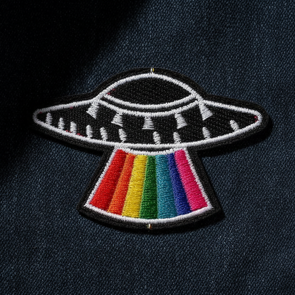 Close-up of an embroidered UFO patch with a rainbow beam on black fabric