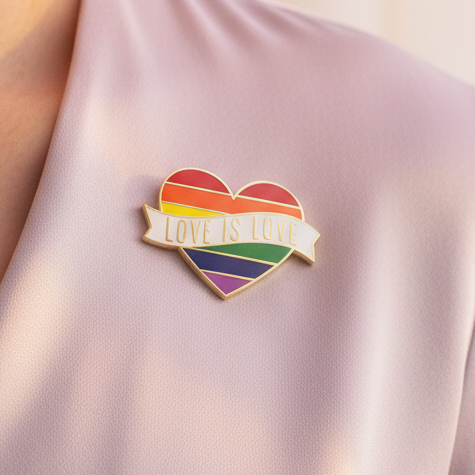 Love Is Love heart enamel pin with rainbow stripes on pale pink fabric