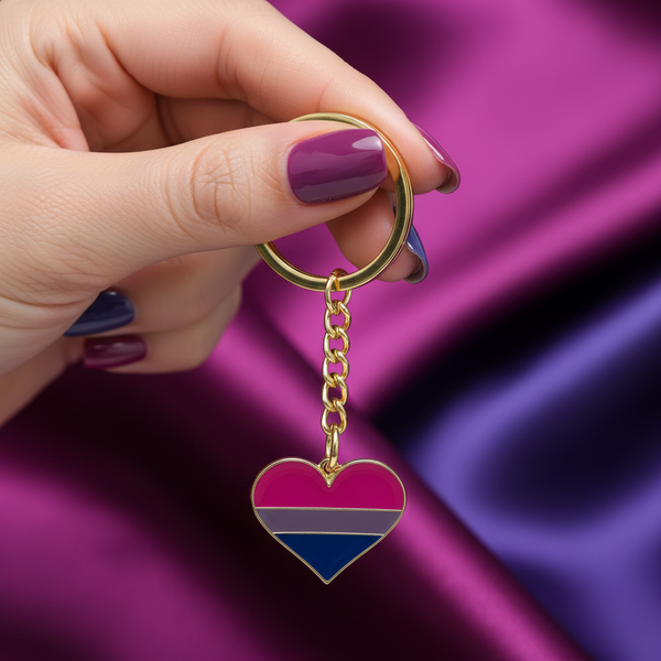 Bisexual pride heart keychain with gold ring and chain, held against a purple background